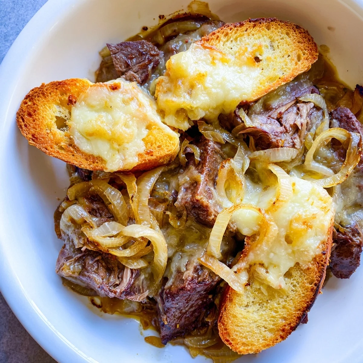 Tender French Onion Pot Roast Casserole with bubbling melted Gruyère cheese and golden-brown baguette.