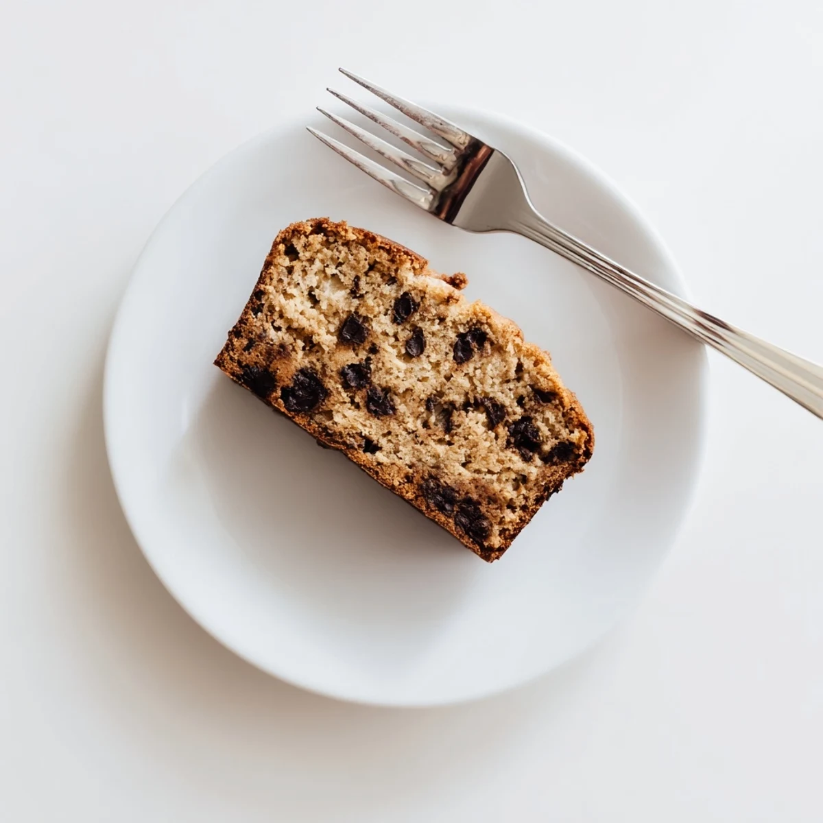 A close-up of freshly baked Banana Bread Variations, showing a moist, golden-brown loaf studded with chocolate chips, sliced on a wooden cutting board.  