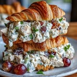 Picnic Chicken Salad Croissant Sandwiches with Grapes on a rustic wooden board, showcasing golden croissants filled with creamy chicken salad and juicy red grapes.
