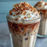 Iced Vanilla Bean Frappuccino with Toasted Coconut Foam in a tall glass, creamy vanilla coffee blended with ice and topped with airy coconut foam and toasted coconut.