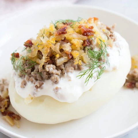 Steaming hot Lithuanian Cepelinai dumplings, filled with savory meat, are served with a creamy bacon sauce.