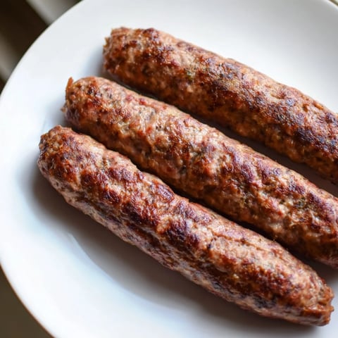 Golden-brown Romanian mici sausages sizzling on a hot grill, ready to be enjoyed with mustard.