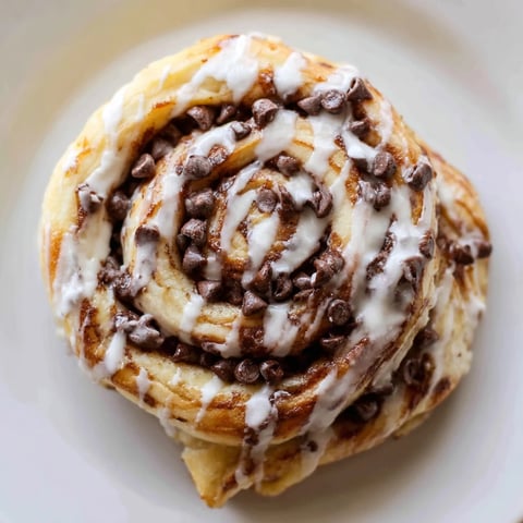 Freshly baked Nutella chocolate chip rolls rest on a cooling rack, revealing gooey swirls of hazelnut spread and melted chips.