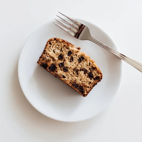 A close-up of freshly baked Banana Bread Variations, showing a moist, golden-brown loaf studded with chocolate chips, sliced on a wooden cutting board.  