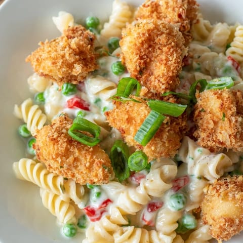 A close-up of crispy fried chicken bites and rotini pasta tossed with fresh herbs in a rich ranch dressing, served in a white bowl.