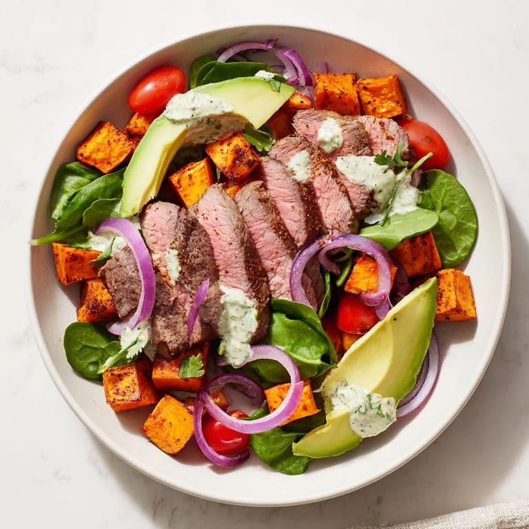 Freshly plated Beef Avocado Sweet Potato Bowl features seared beef resting on greens with vibrant toppings.