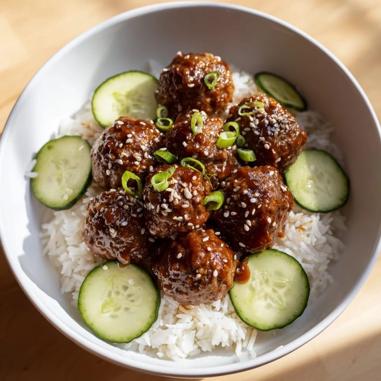 A close-up of vibrant teriyaki meatball bowls with sesame seeds and fresh cucumber slices on top.