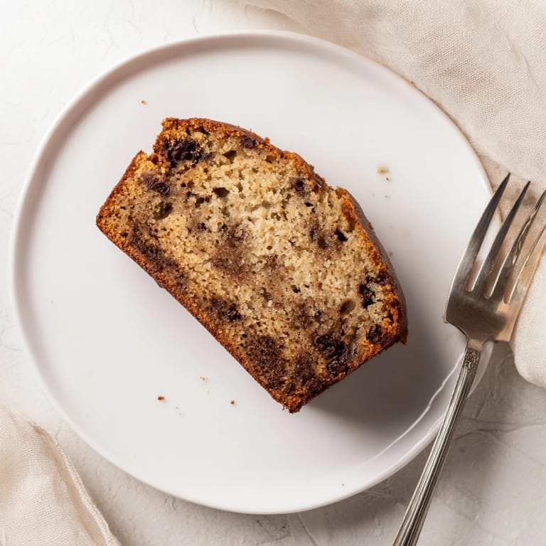 A rustic loaf pan of Banana Bread Variations, featuring a crackled, golden top with chopped walnuts, served alongside a cup of coffee for an inviting breakfast.