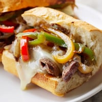Golden-brown Philly Cheesesteak Grilled Cheese sandwiches with melted provolone, sautéed peppers, and onions on a wooden board.
