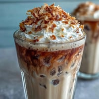 Iced Vanilla Bean Frappuccino with Toasted Coconut Foam in a tall glass, creamy vanilla coffee blended with ice and topped with airy coconut foam and toasted coconut.