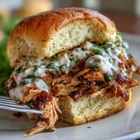 Smoked pulled chicken sandwiches with white BBQ sauce piled high on soft buns for a tangy Southern twist. Juicy, tender smoked chicken thighs shredded and coated in creamy Alabama-style white BBQ sauce. Smoky pulled chicken sandwiches topped with crunchy coleslaw and zesty white BBQ sauce for a perfect balance of flavors.